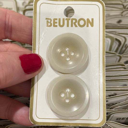 Hand holding a package of Beutron buttons with red nail polish.