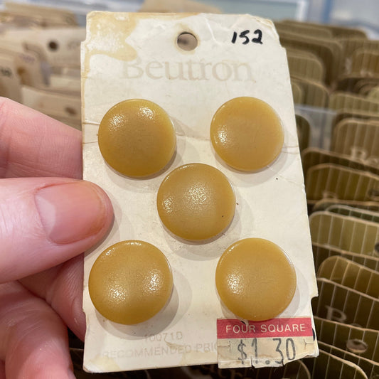 Hand holding a package of beige buttons with a blurred background