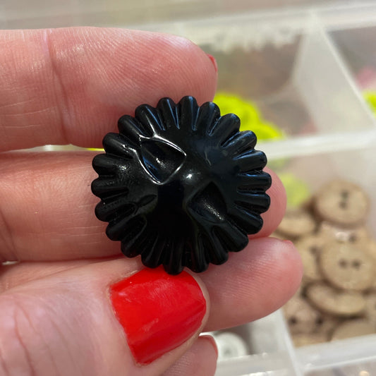 Black floral hair clip held by a hand with red nail polish, against a background of colorful buttons.