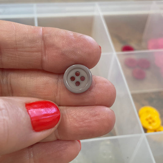 Hand holding a button with a container of buttons in the background