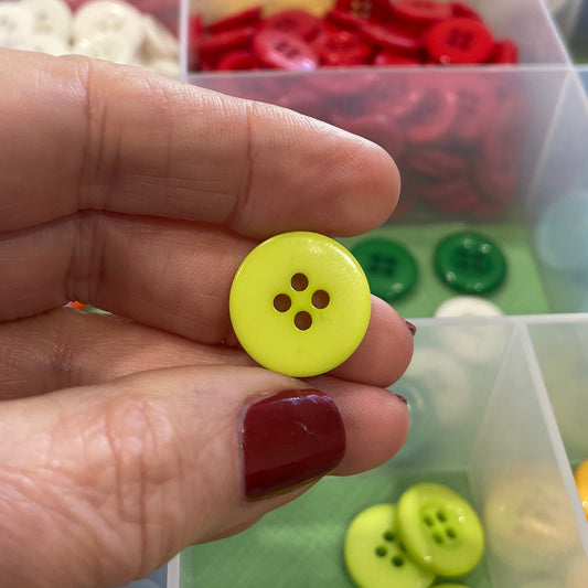 Hand holding a yellow button with a background of assorted buttons in a container