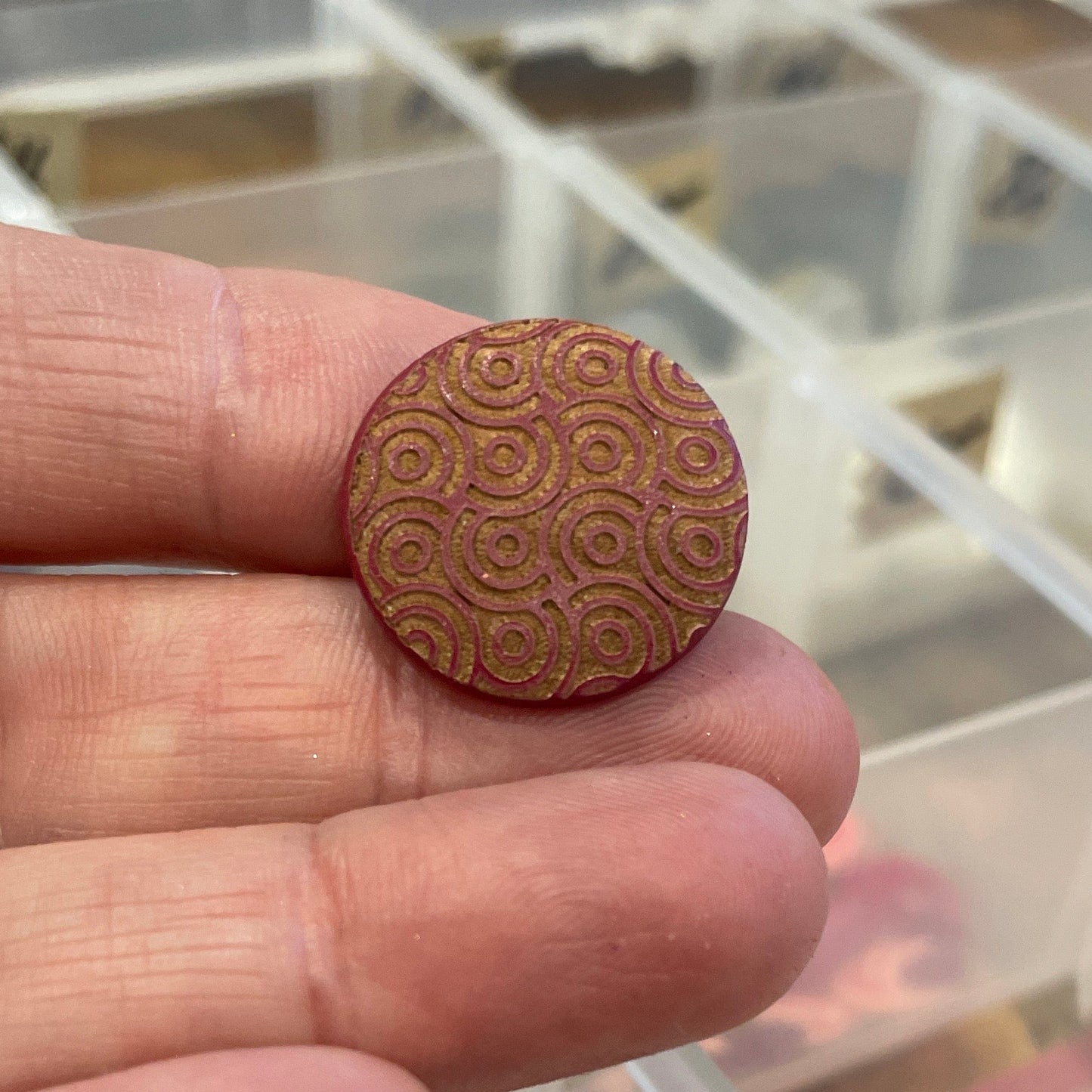 Wooden button held between fingers with a clear plastic organizer in the background