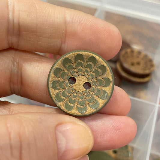 Hand holding a decorative button with a container of similar buttons in the background