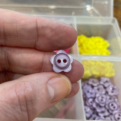 Hand holding a small pink button with a container of colorful buttons in the background