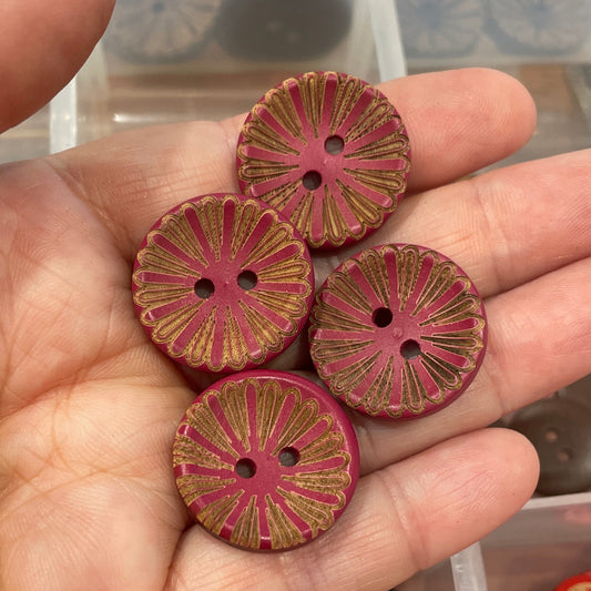 Hand holding red and gold buttons with a container of various buttons in the background