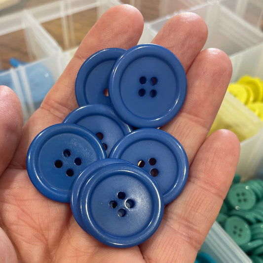Blue buttons held in a hand with a container of buttons in the background