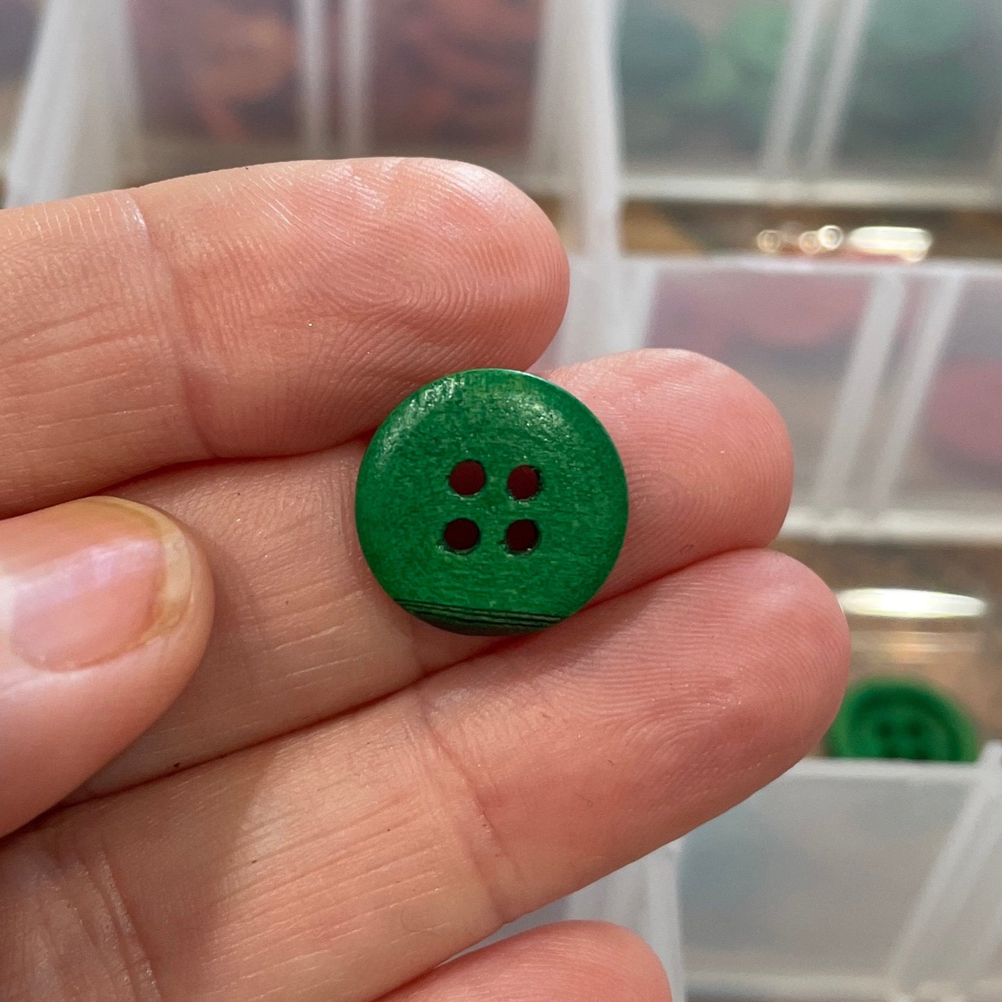 Hand holding a green button with a clear container of buttons in the background