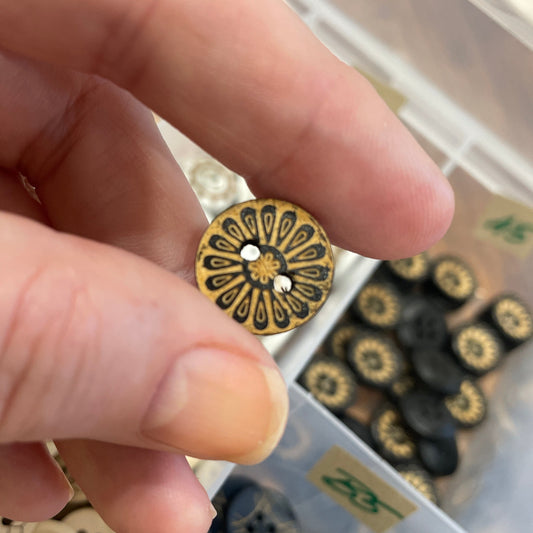 Hand holding a decorative button with a background of various buttons in a box.