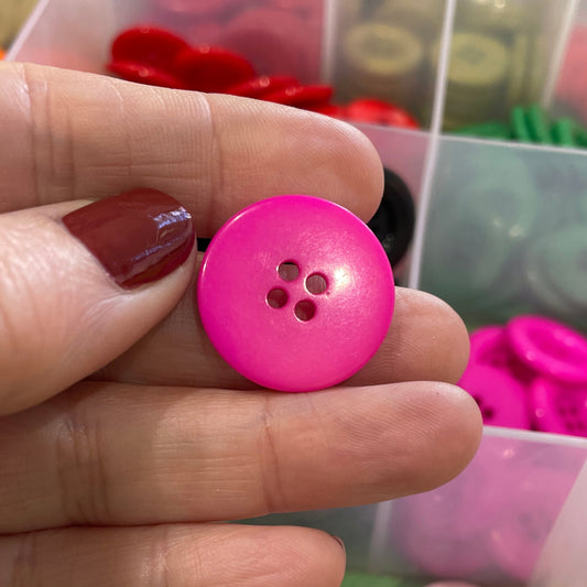 Hand holding a pink button with a clear container of assorted buttons in the background