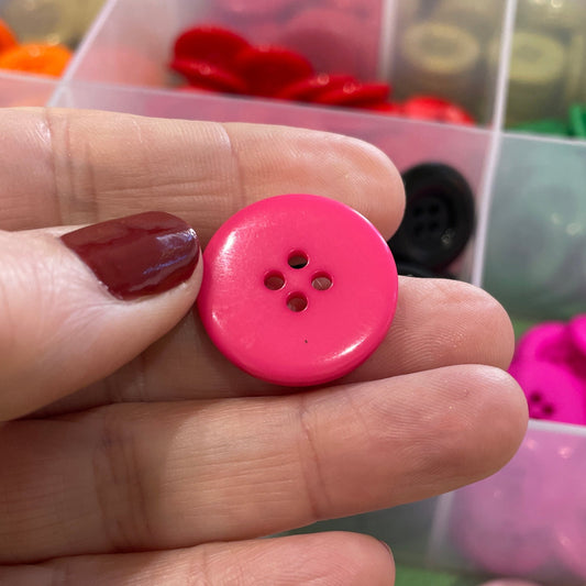 Pink button held by a hand with a colorful button collection in the background