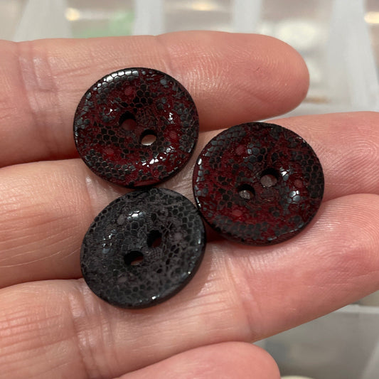 Three dark-colored buttons held between fingers with a container of buttons in the background.