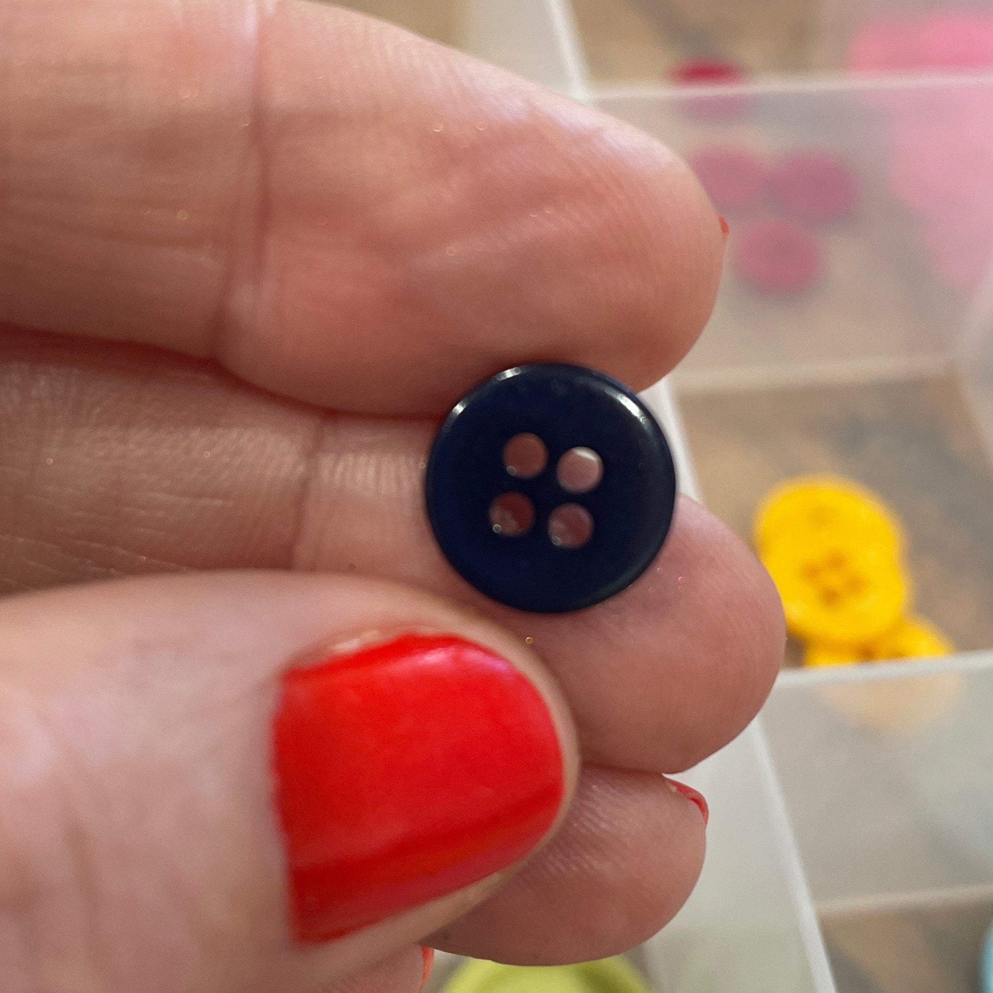 Hand holding a blue button with a clear container of buttons in the background