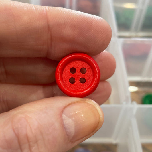 Red button held by a hand with a background of button storage organizer.