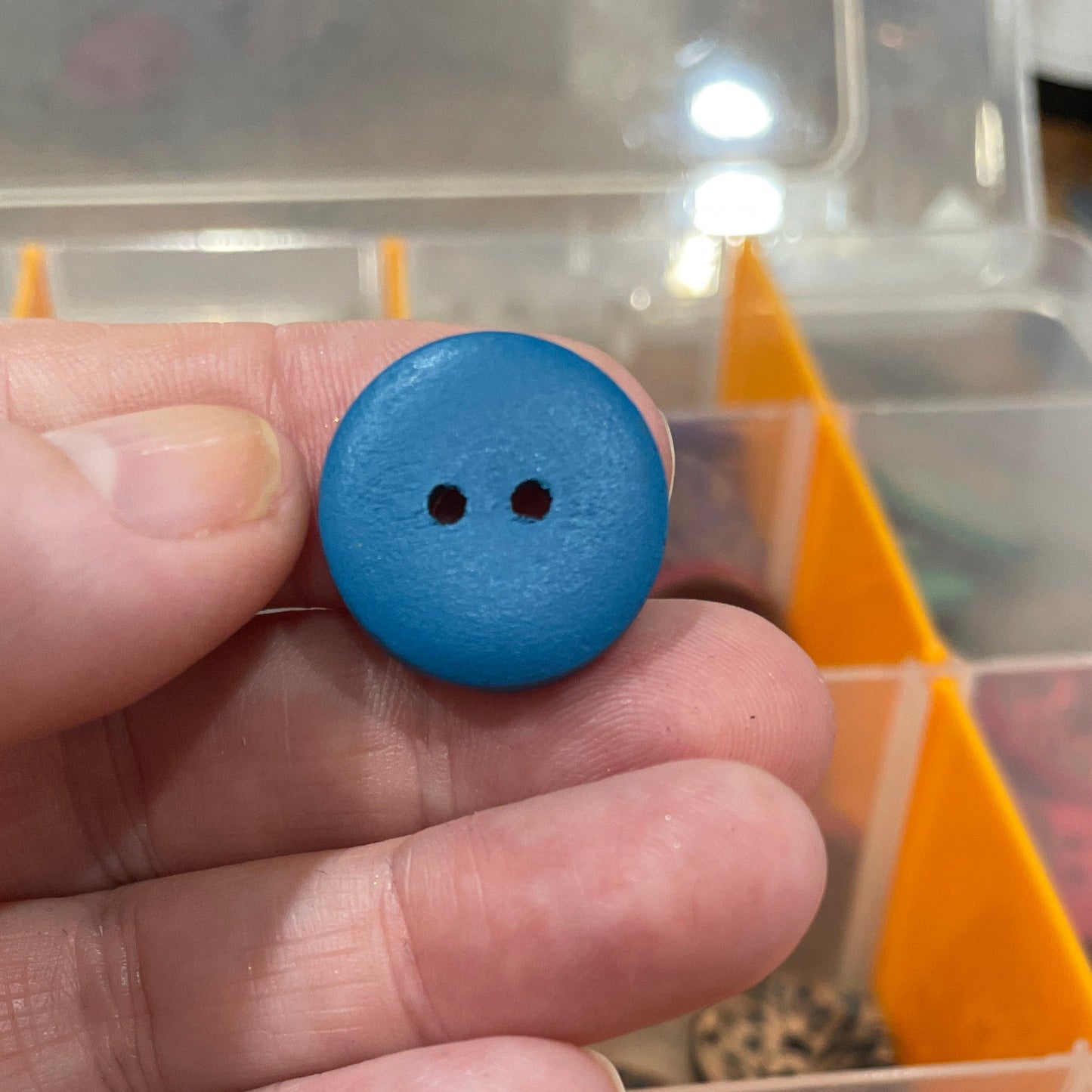 Hand holding a blue button with a container of buttons in the background