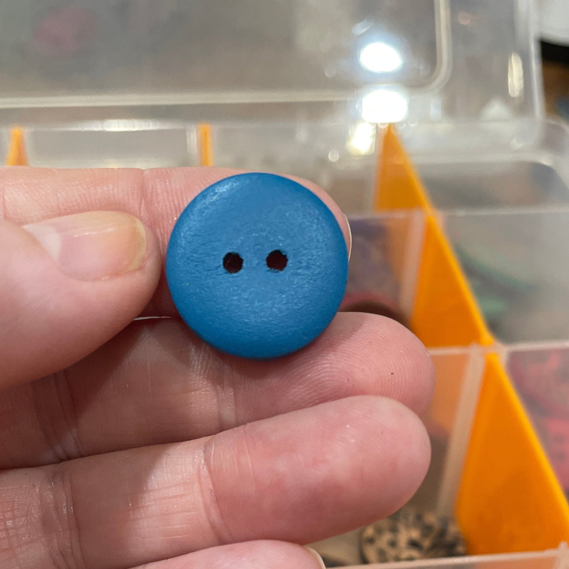 Hand holding a blue button with a container of buttons in the background