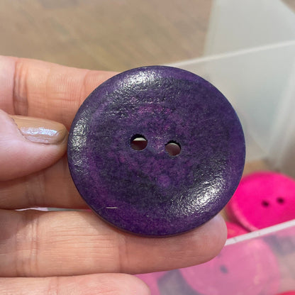 Purple button held in a hand with pink buttons in the background