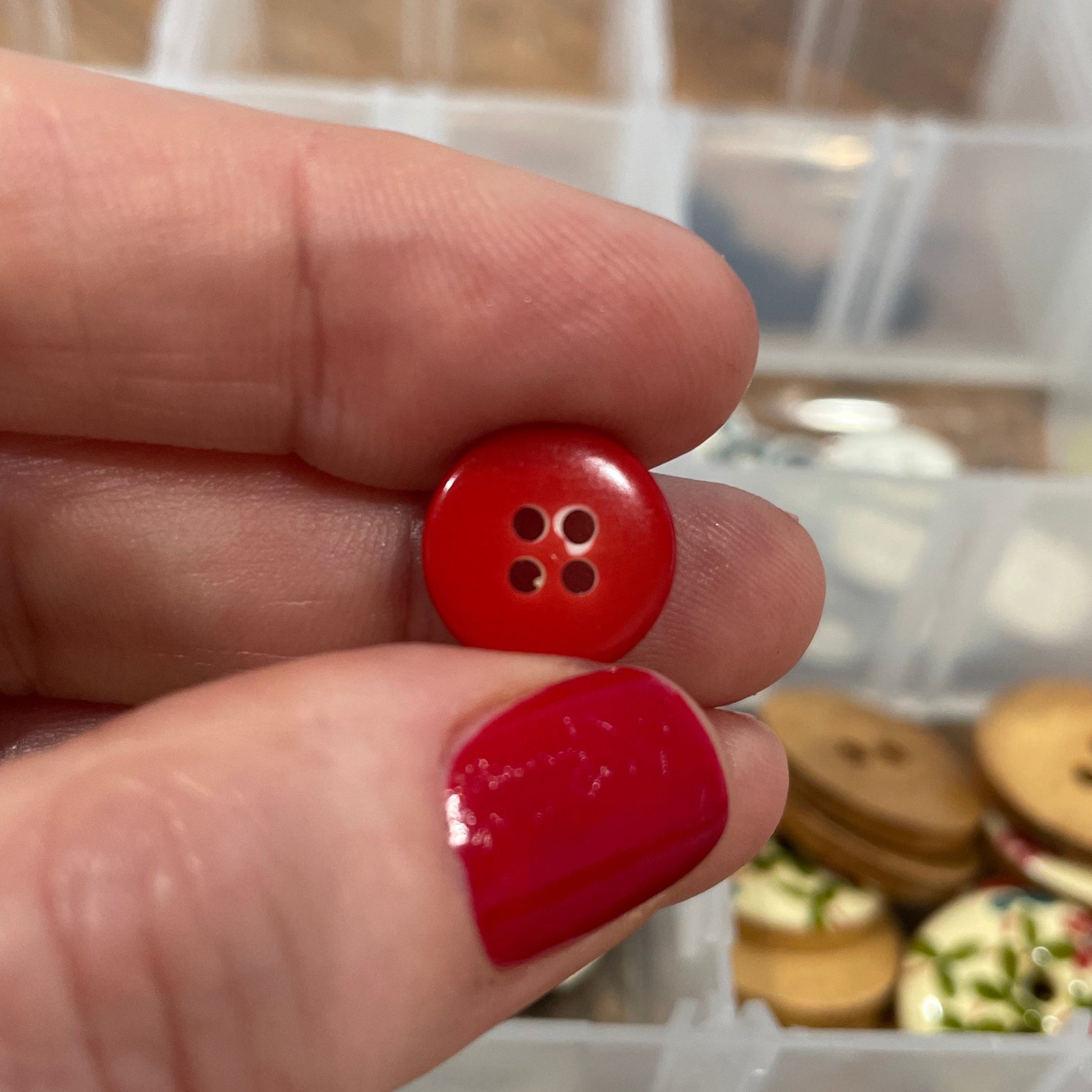 Red button held between two fingers with a container of buttons in the background