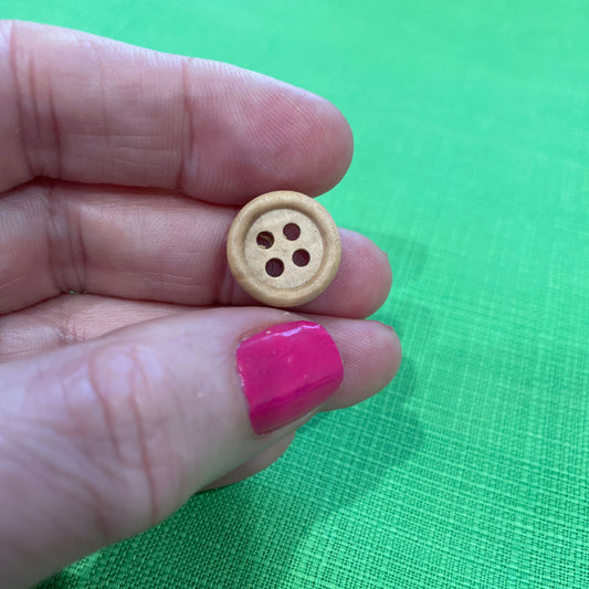 Small wooden button held between two fingers against a green fabric background