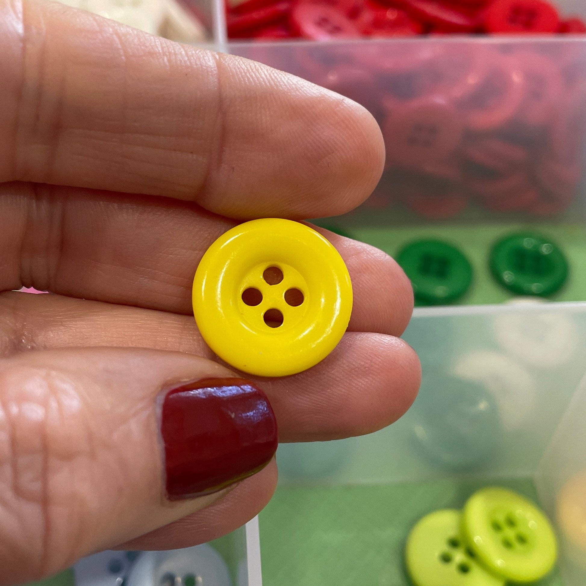 Hand holding a yellow button with a colorful button organizer in the background