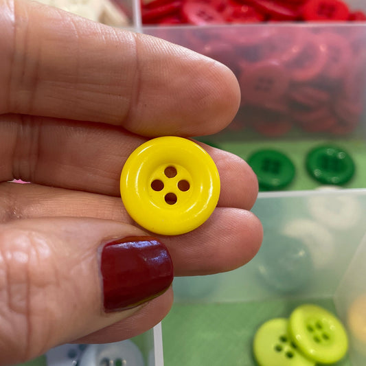 Hand holding a yellow button with a colorful button organizer in the background