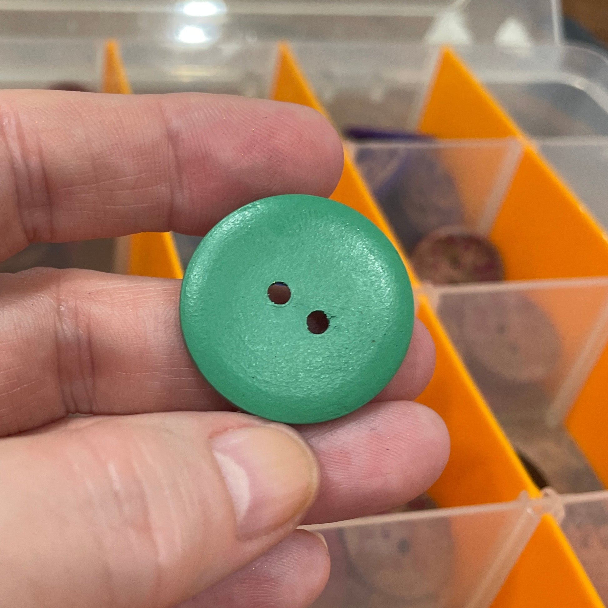 Hand holding a green button with a blurred background of a storage box with compartments.