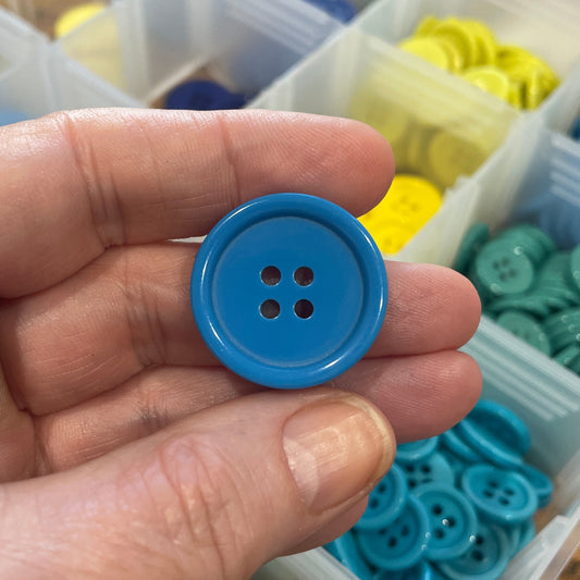 Hand holding a blue button with a container of buttons in the background