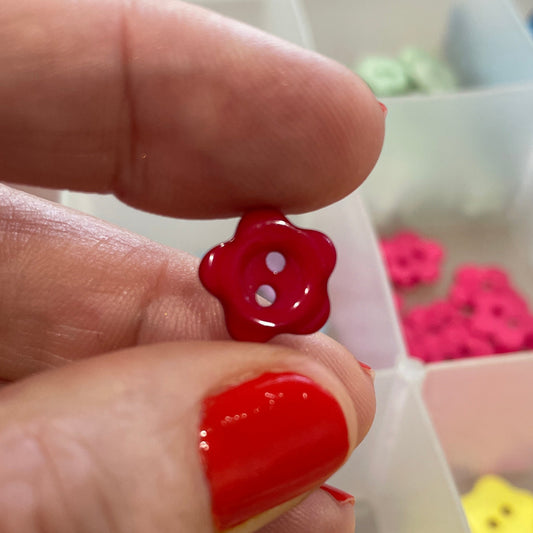 Hand holding a red button with a background of various buttons in a box.