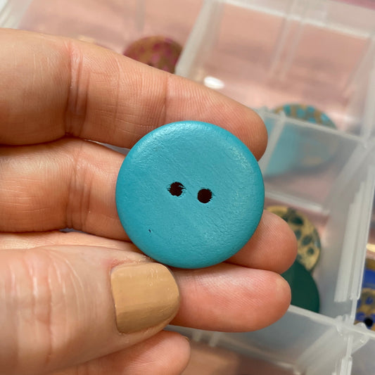Hand holding a blue button with a container of buttons in the background