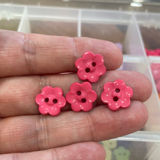 Three pink flower-shaped buttons held between fingers with a blurred background