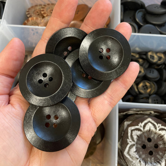 Hand holding black buttons with a clear container of buttons in the background