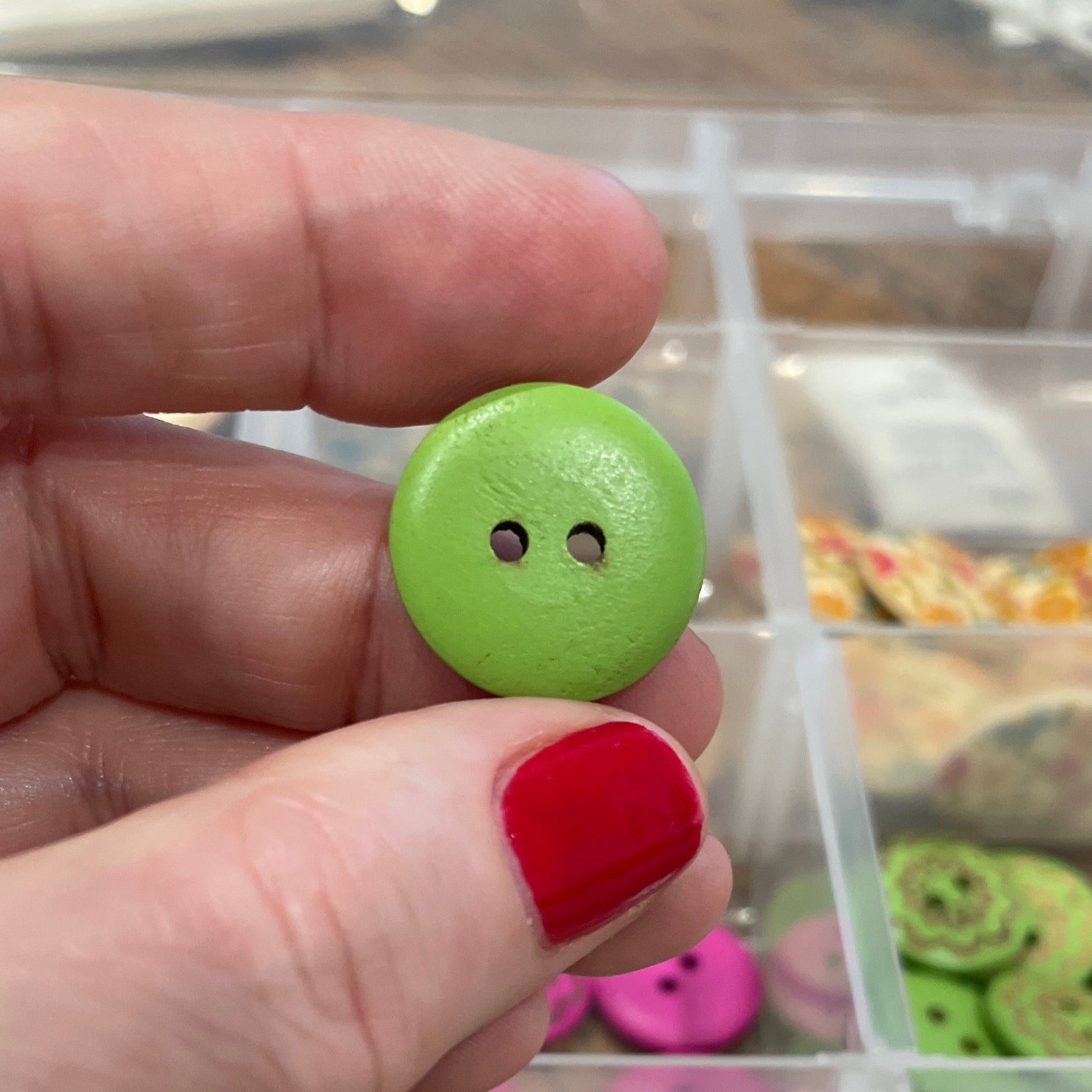 Hand holding a green button with a clear container of buttons in the background