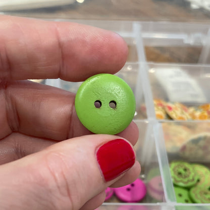 Hand holding a green button with a clear container of buttons in the background