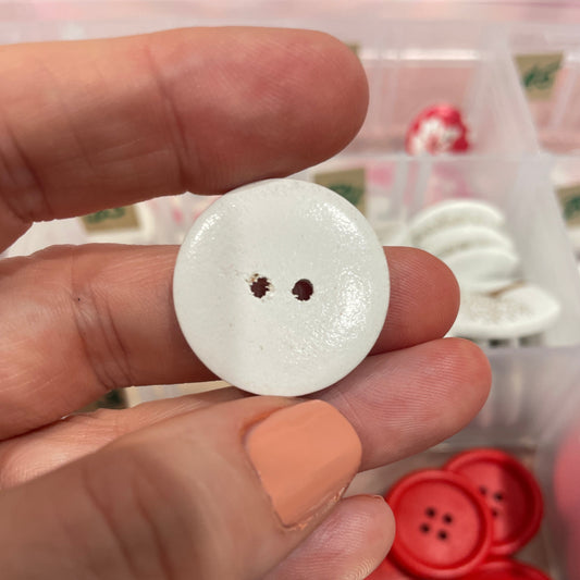 White button held by a hand with a container of buttons in the background