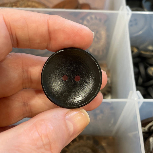 Hand holding a black button with a container of buttons in the background