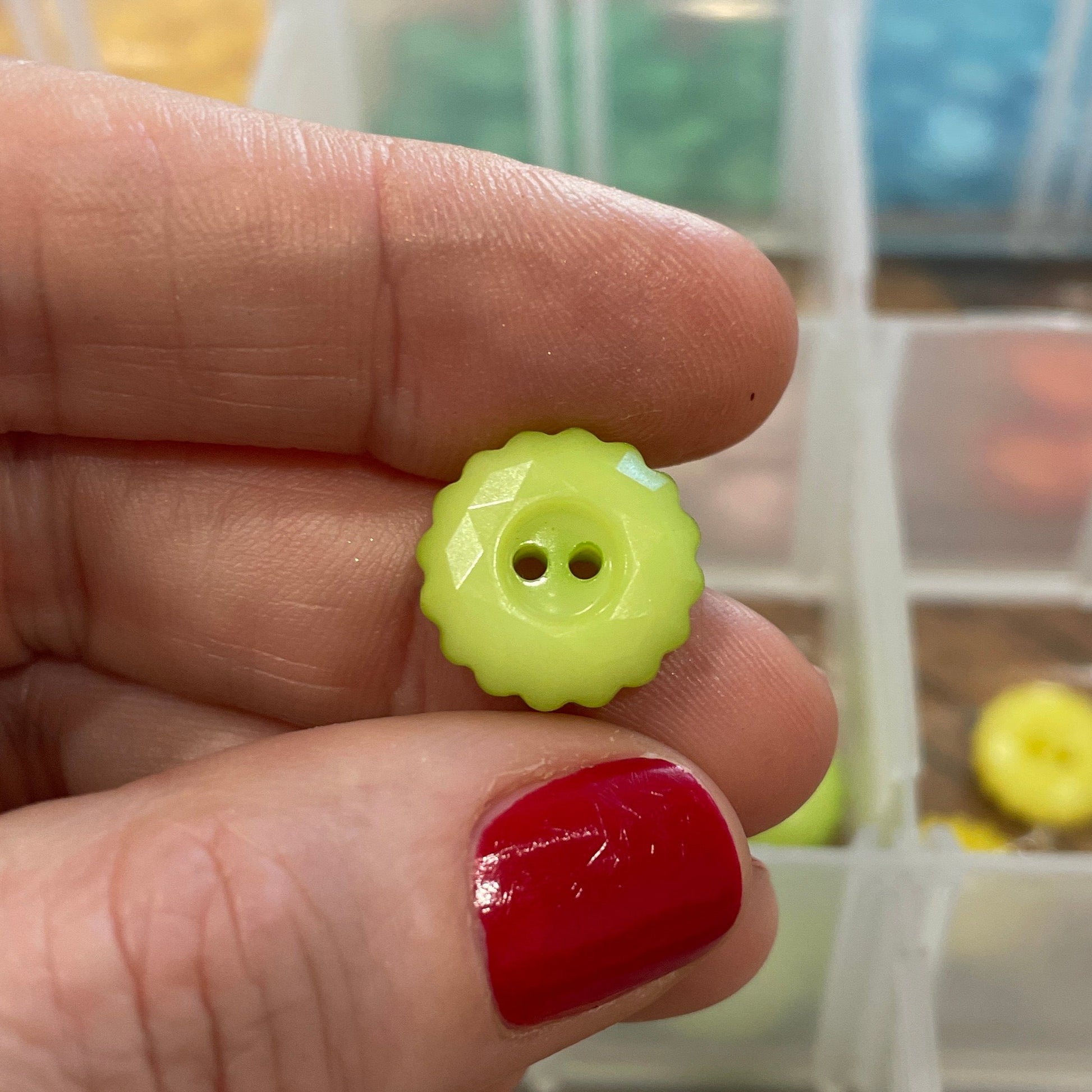 Hand holding a yellow button with a clear container of buttons in the background