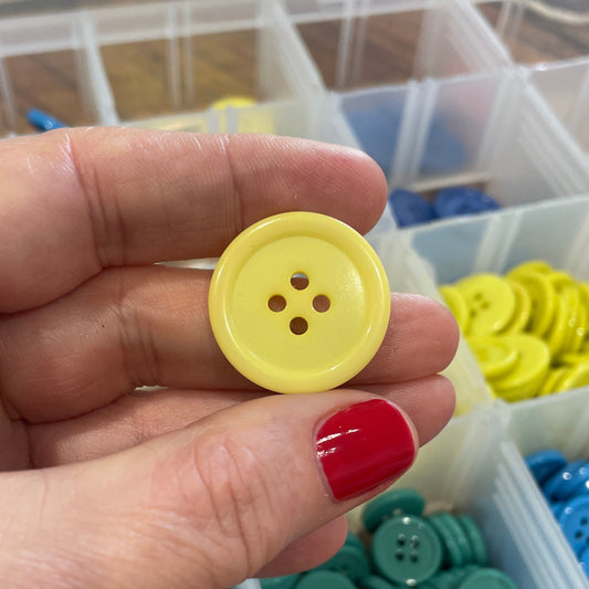 Hand holding a yellow button with a container of assorted buttons in the background