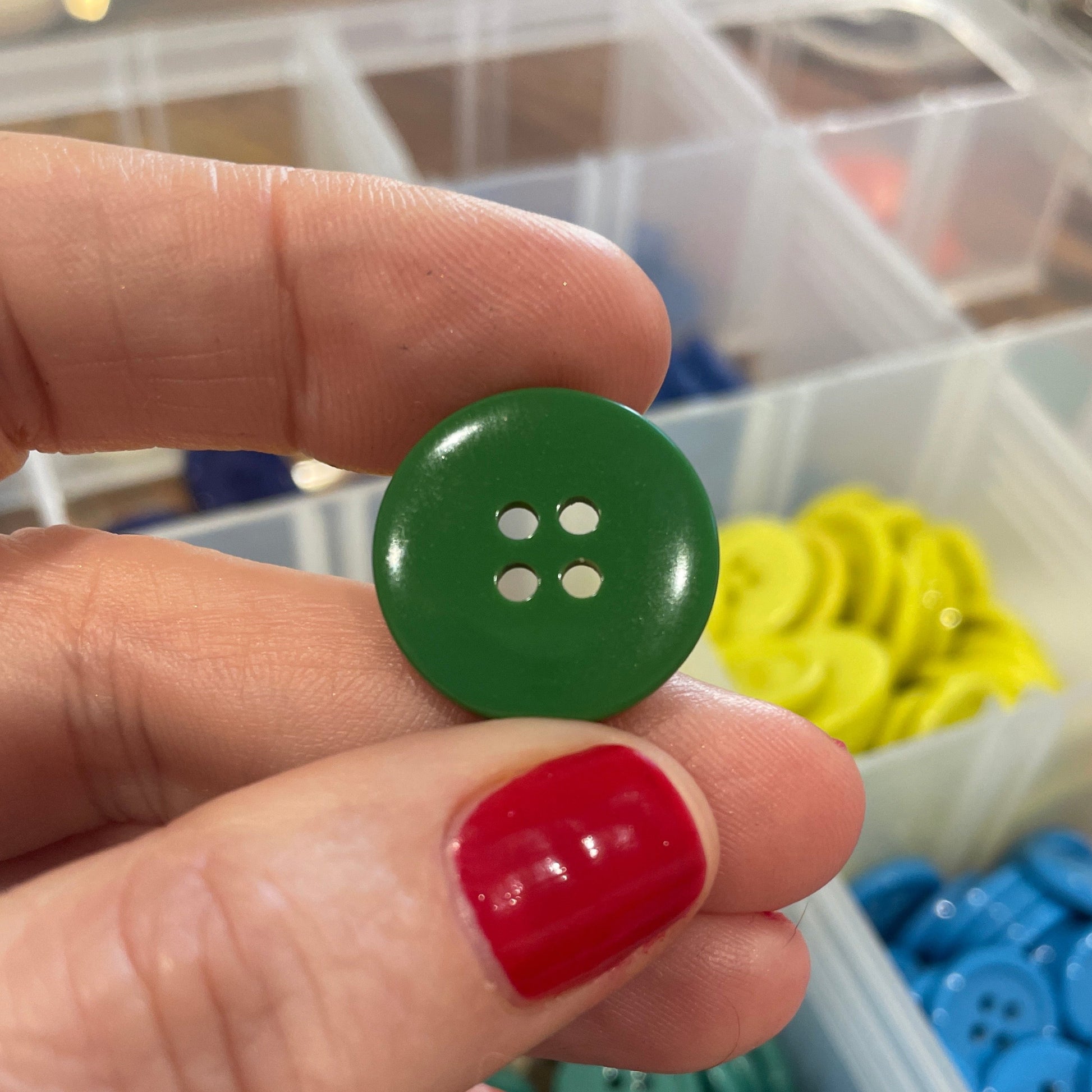 Hand holding a green button with a container of buttons in the background