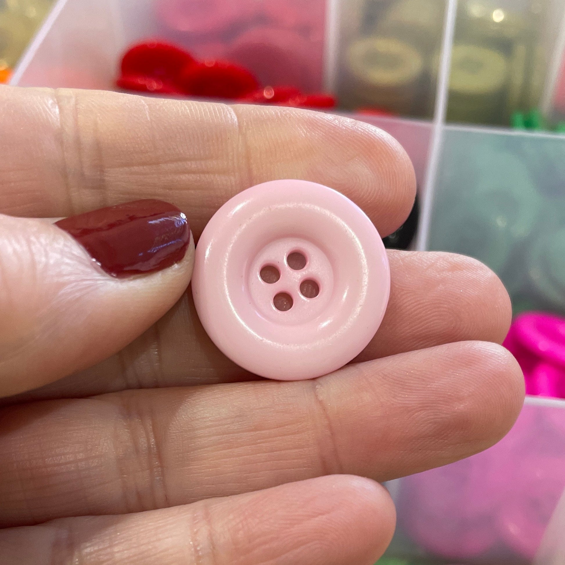 Pink button held between fingers with a colorful button organizer in the background