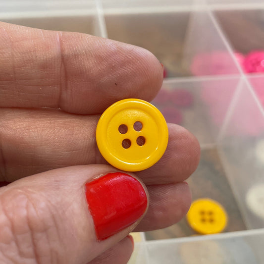 Hand holding two colorful buttons with a container of buttons in the background