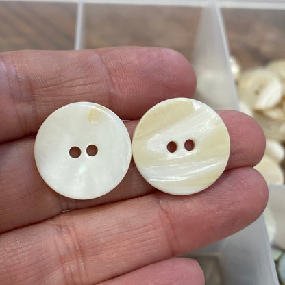 Two white buttons held between fingers with a container of buttons in the background