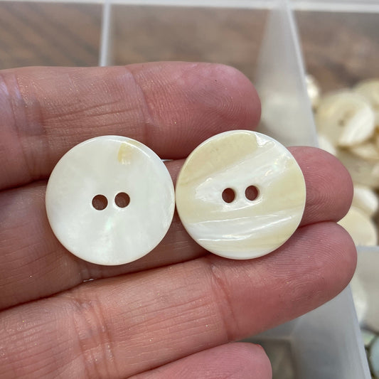 Two white buttons held between fingers with a container of buttons in the background