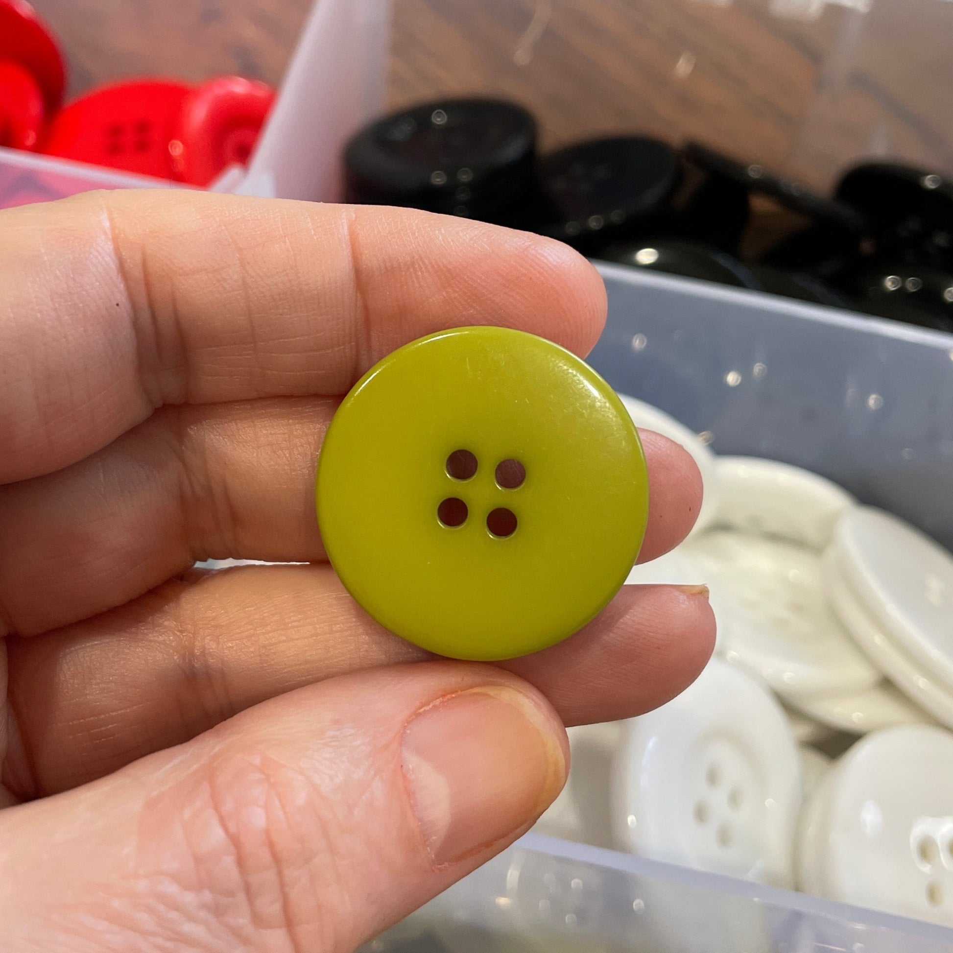 Hand holding a green button with a container of buttons in the background