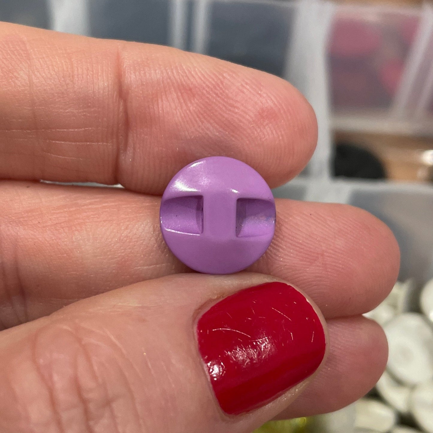 Hand holding two small round buttons, one purple and one red, with a container of buttons in the background.