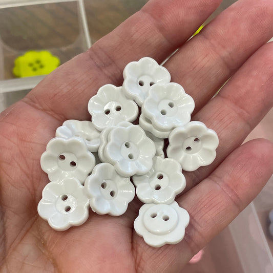 Hand holding white flower-shaped buttons with a container of buttons in the background