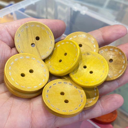 Hand holding yellow buttons with a container of pink buttons in the background