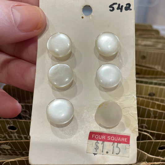 Set of pearl buttons on a card held by a hand with a blurred background