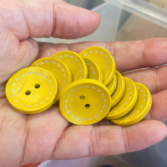 Hand holding yellow buttons with a container of various colored buttons in the background.