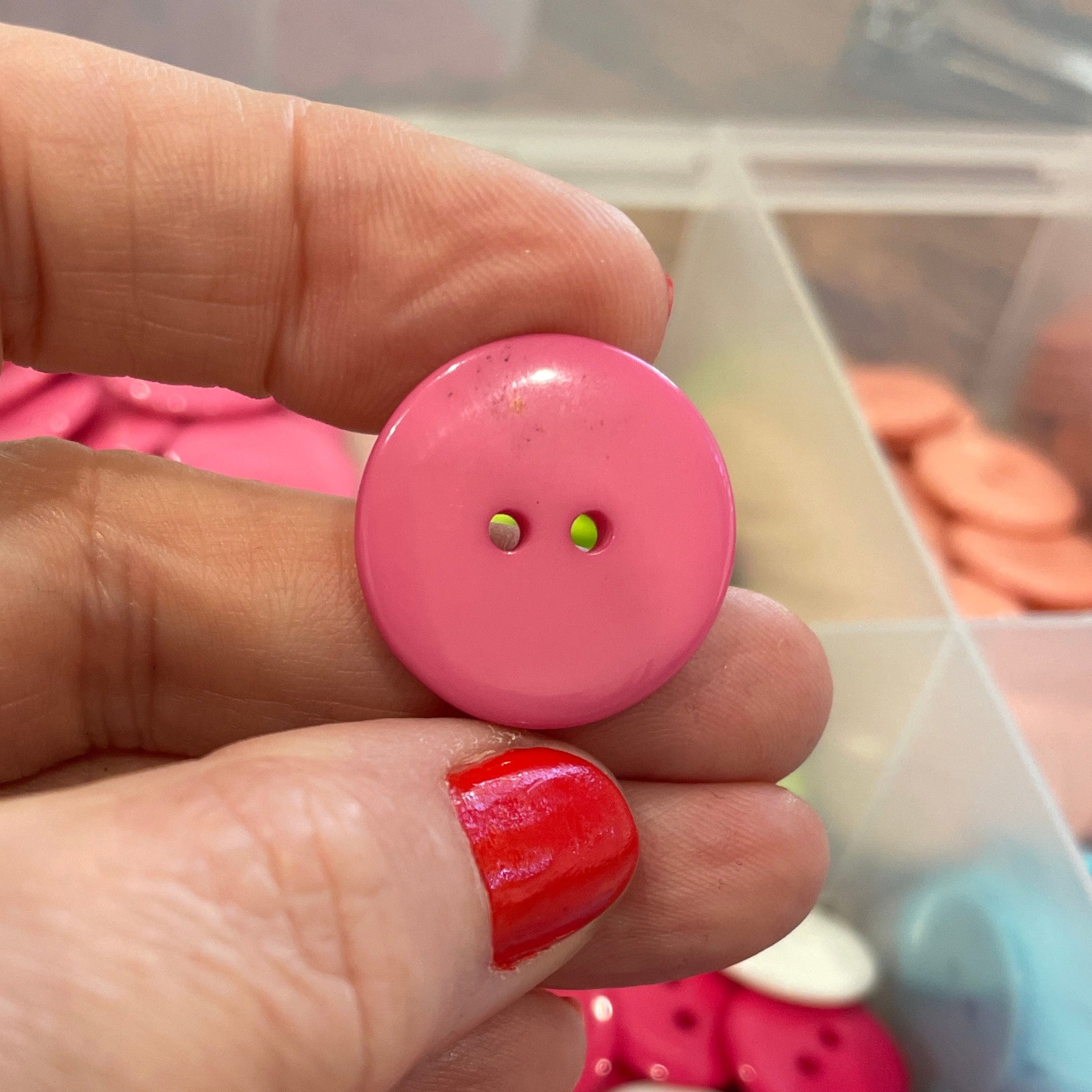 Hand holding a pink button with a container of colorful buttons in the background