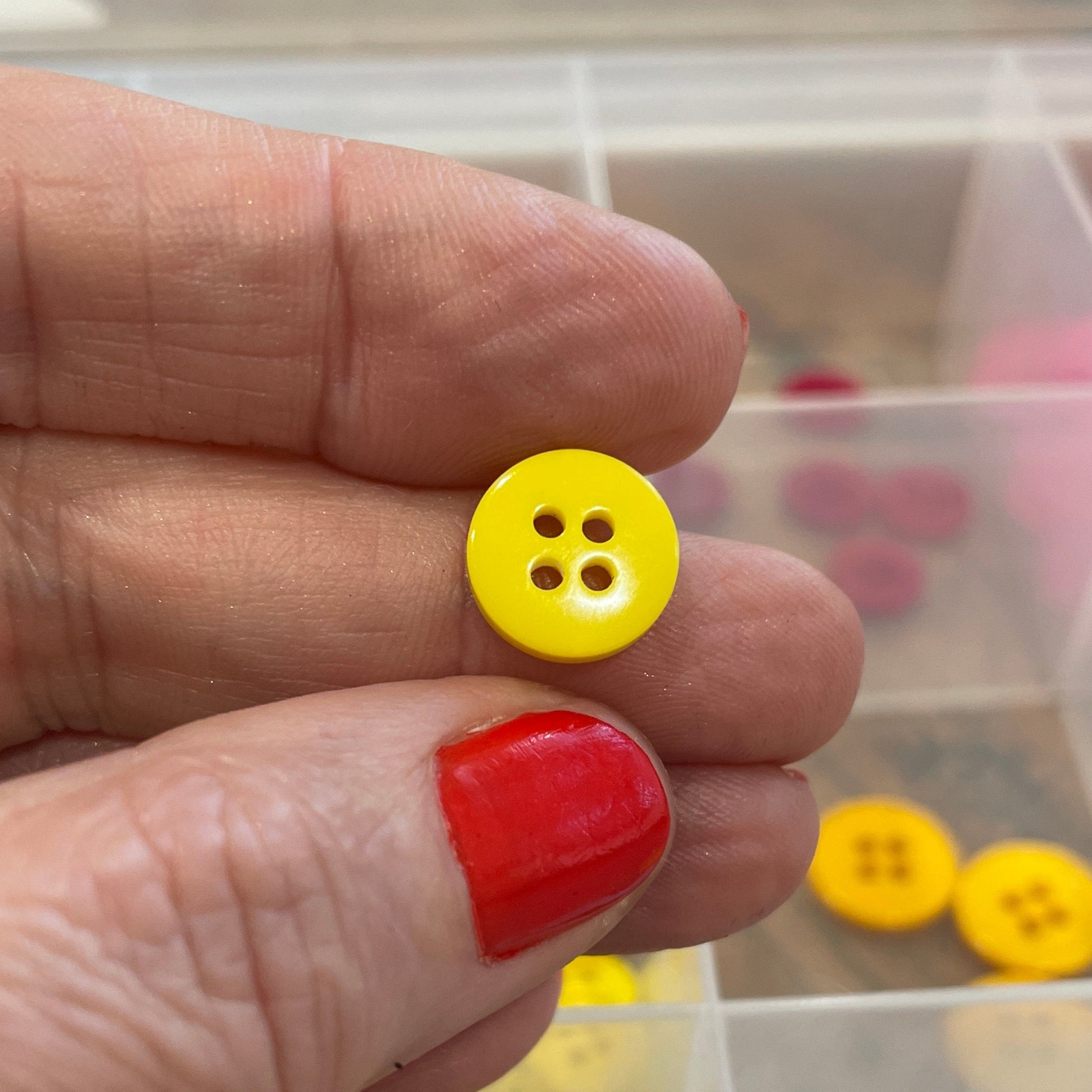 Hand holding a yellow button with a clear container of buttons in the background