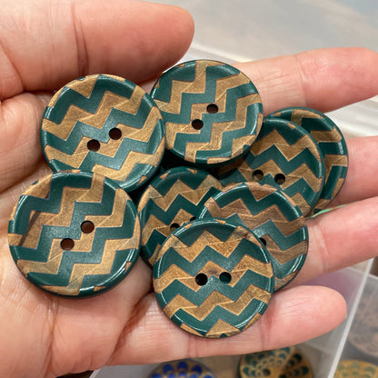 Hand holding decorative buttons with a box of more buttons in the background